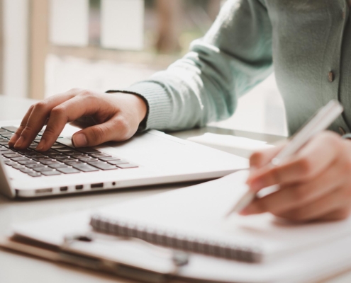 Person using laptop and writing in checklist