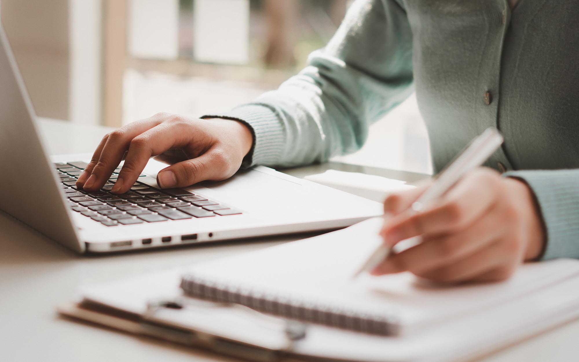 Person using laptop and writing in checklist